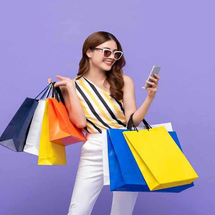 Woman holding multiple colorful shopping bags and a phone against a purple background